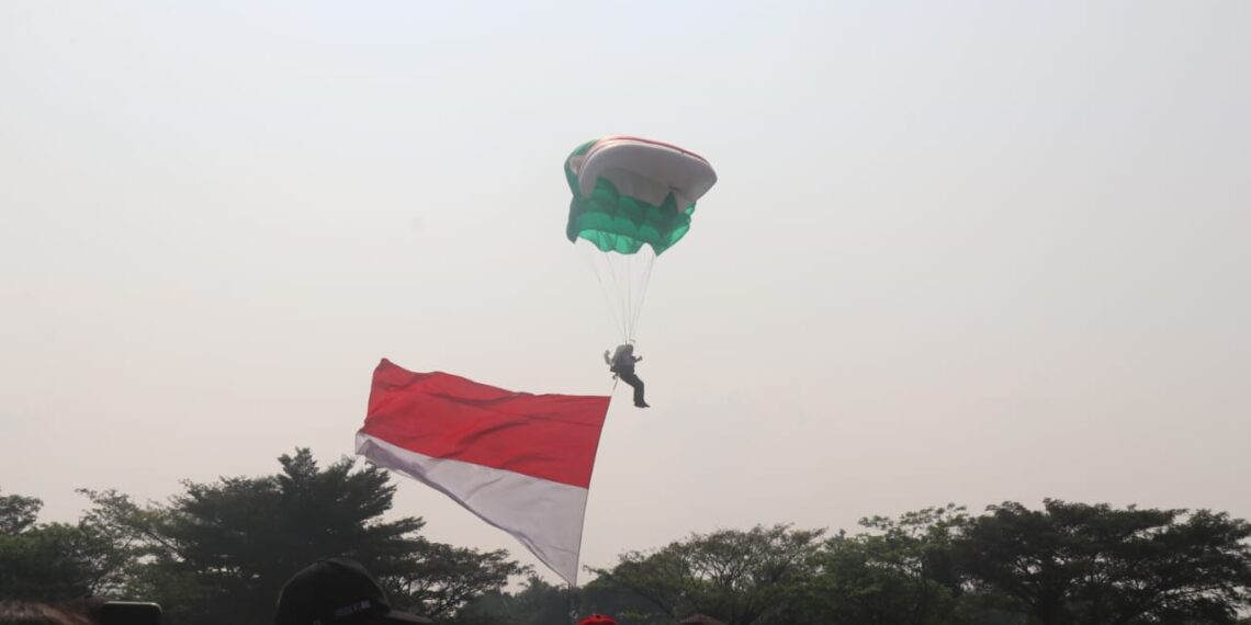 Pemerintah Kabupaten (Pemkab) Bogor menyuguhkan atraksi terjun payung yang membawa bendera merah putih, bendera Kabupaten Bogor, dan bendera KONI Kabupaten Bogor kepada masyarakat pada Minggu (11/8/24). (FOTO: Humas Pemkab Bogor)