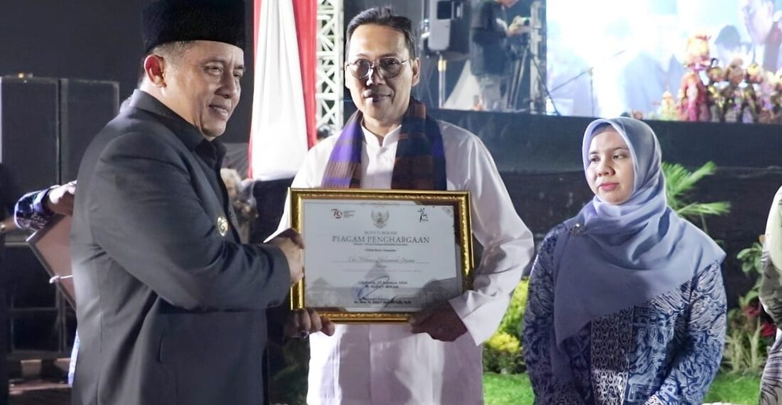 Penjabat (Pj) Bupati Bekasi, Dedy Supriyadi, menyerahkan hadiah kepada Eko Wibowo Yuliatmoko sebagai pemenang Lomba Desain Logo Hari Jadi Kabupaten Bekasi ke-74. Acara penyerahan hadiah berlangsung pada malam tasyakuran penutup rangkaian Hari Jadi Kabupaten Bekasi ke-74, di Plaza Pemda Cikarang Pusat, Jumat (22/8/2024).(FOTO: Humas Pemkab Bekasi)