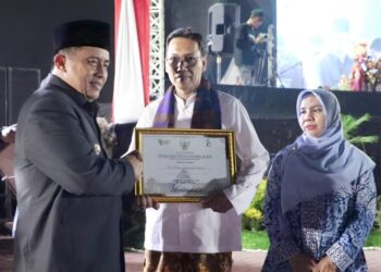 Penjabat (Pj) Bupati Bekasi, Dedy Supriyadi, menyerahkan hadiah kepada Eko Wibowo Yuliatmoko sebagai pemenang Lomba Desain Logo Hari Jadi Kabupaten Bekasi ke-74. Acara penyerahan hadiah berlangsung pada malam tasyakuran penutup rangkaian Hari Jadi Kabupaten Bekasi ke-74, di Plaza Pemda Cikarang Pusat, Jumat (22/8/2024).(FOTO: Humas Pemkab Bekasi)