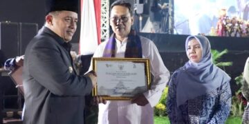 Penjabat (Pj) Bupati Bekasi, Dedy Supriyadi, menyerahkan hadiah kepada Eko Wibowo Yuliatmoko sebagai pemenang Lomba Desain Logo Hari Jadi Kabupaten Bekasi ke-74. Acara penyerahan hadiah berlangsung pada malam tasyakuran penutup rangkaian Hari Jadi Kabupaten Bekasi ke-74, di Plaza Pemda Cikarang Pusat, Jumat (22/8/2024).(FOTO: Humas Pemkab Bekasi)