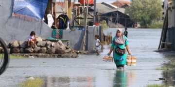Warga berjalan menerobos banjir rob yang merendam pemukiman. (Dok. Istimewa)